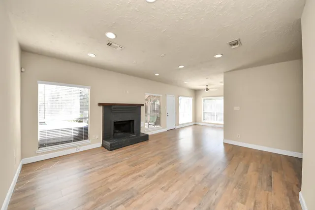 an empty room with wooden floor fireplace and windows