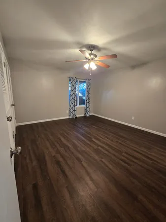 an empty room with wooden floor fan and windows
