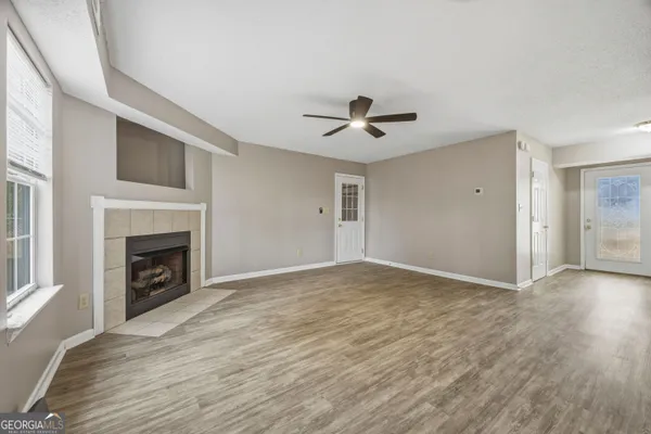 a view of an empty room with wooden floor fireplace and a window