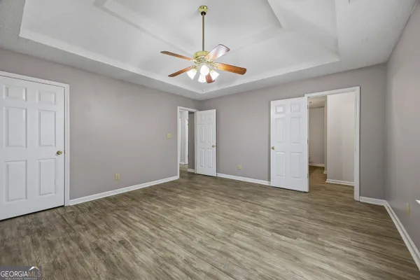 a view of an empty room with chandelier fan and wooden floor