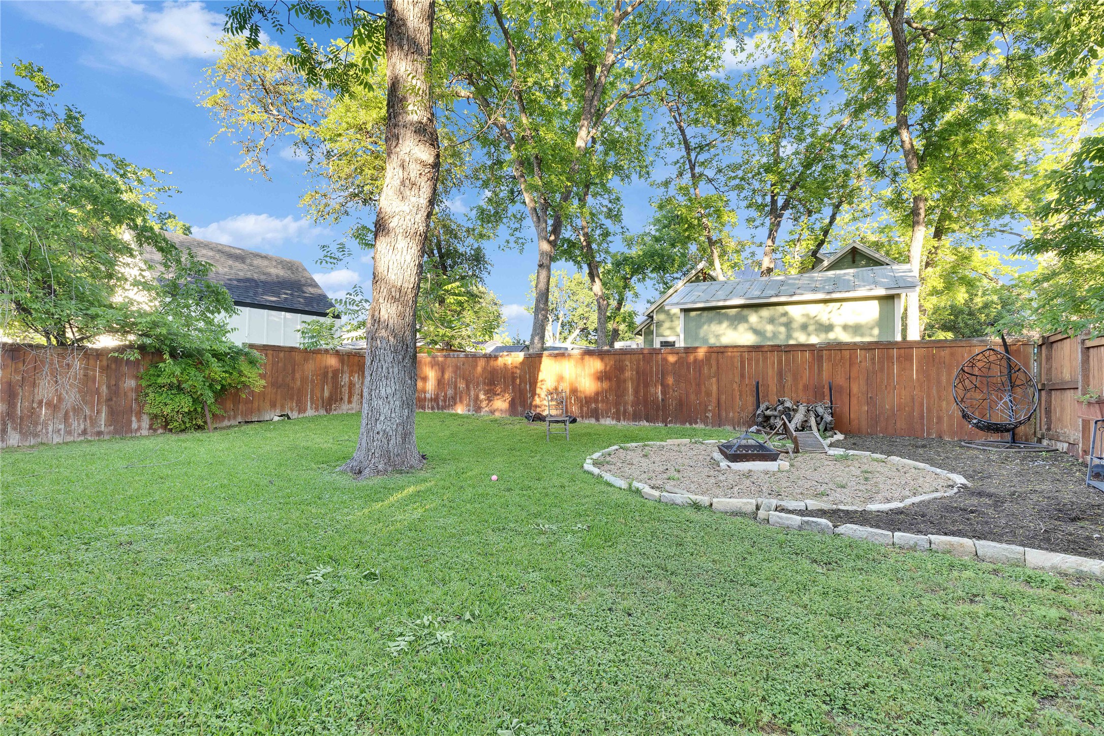 4607 Evans Avenue, Unit B Austin, TX 78751 - Photo 27 of 34 Expansive backyard featuring a large tree, full wood privacy fencing, and a stone-lined garden bed with a fire pit