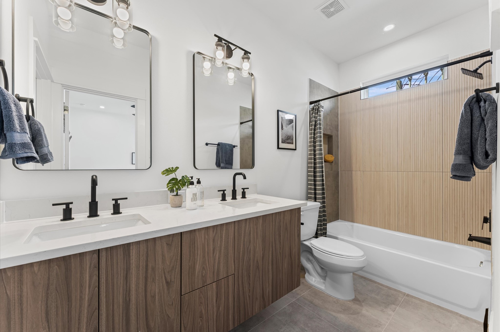 2424 Freeman Street Houston, TX 77009 - Photo 7 of 43 This stylish first-floor bathroom features a tub/shower combo, sleek modern tile, and a vanity with quartz countertops, combining functionality and contemporary design for family members or guests.