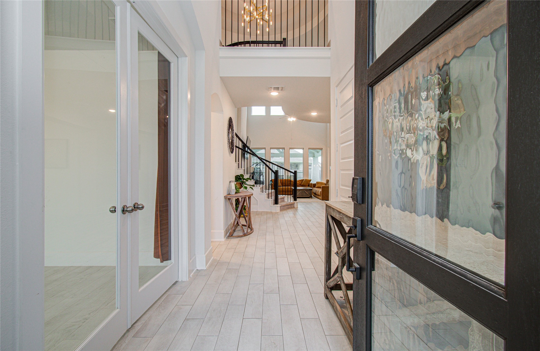 4211 Limestone Terrace Manvel, TX 77578 - Photo 3 of 33 This inviting entryway features a glass-paneled door opening into a bright, spacious hallway with wood-like tile flooring. The area includes a view of a modern staircase, high ceilings, and an open living space with large windows, creating an airy and welcoming atmosphere.