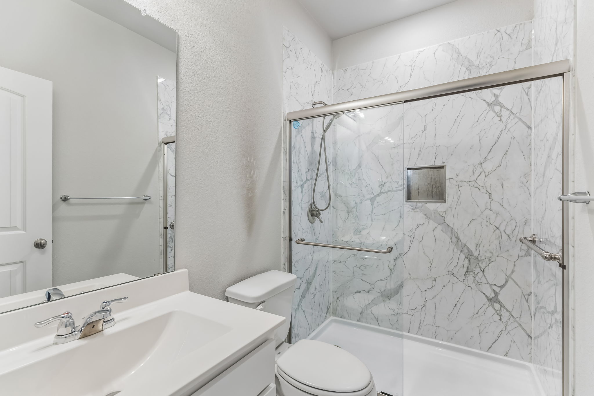 4009 Milano River Road Hutto, TX 78634 - Photo 26 of 40 A modern glass shower enclosure with marble-patterned surrounds anchors this clean bathroom space.