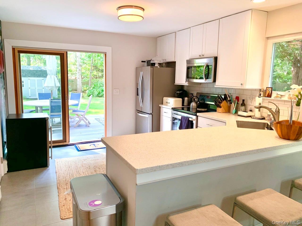 61 Kings Point Road East Hampton, NY 11937 - Photo 2 of 15 Kitchen featuring appliances with stainless steel finishes, backsplash, a kitchen breakfast bar, a peninsula, and white cabinetry