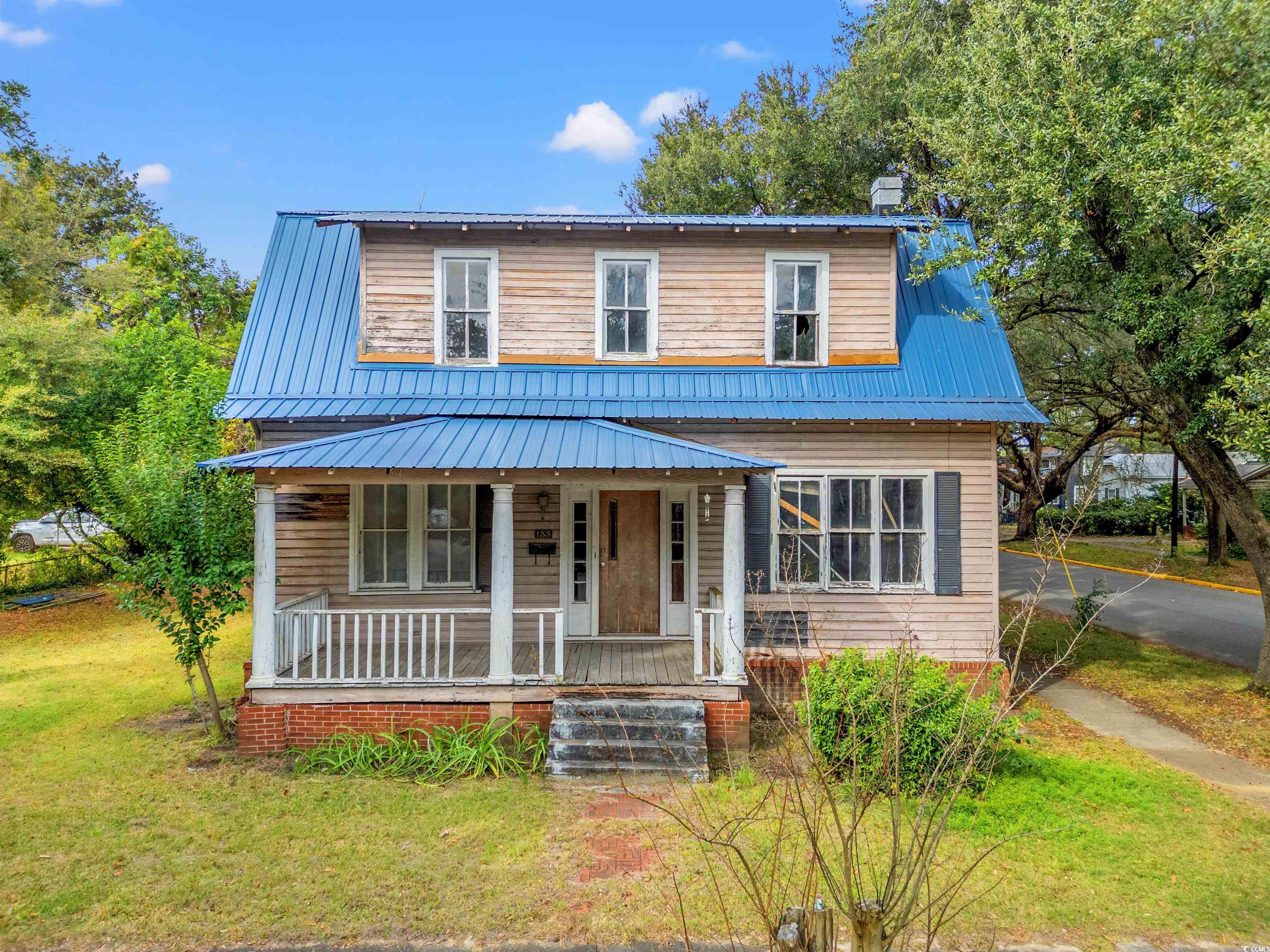 View of front of house featuring a metal roof, a porch, a front yard, and a chimney