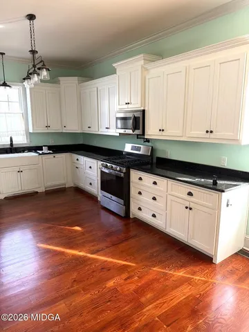 a kitchen with granite countertop a stove a sink and white cabinets