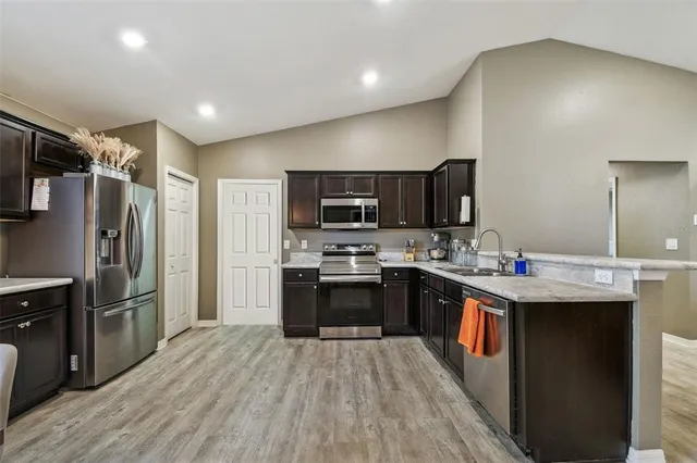 a kitchen with stainless steel appliances kitchen island granite countertop a refrigerator a sink dishwasher a stove and a refrigerator with wooden floor