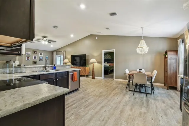 a kitchen with stainless steel appliances granite countertop a stove top oven a sink dishwasher a dining table and chairs with wooden floor