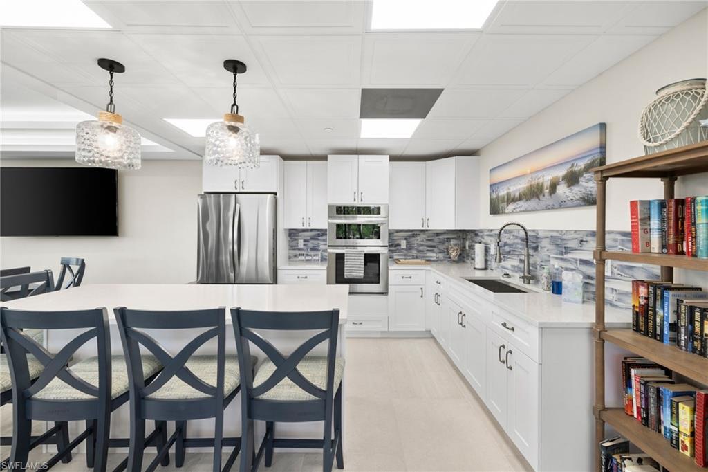 11 Bluebill Avenue, Unit 702 Naples, FL 34108 - Photo 27 of 35 a kitchen with stainless steel appliances kitchen island granite countertop a table chairs refrigerator and microwave