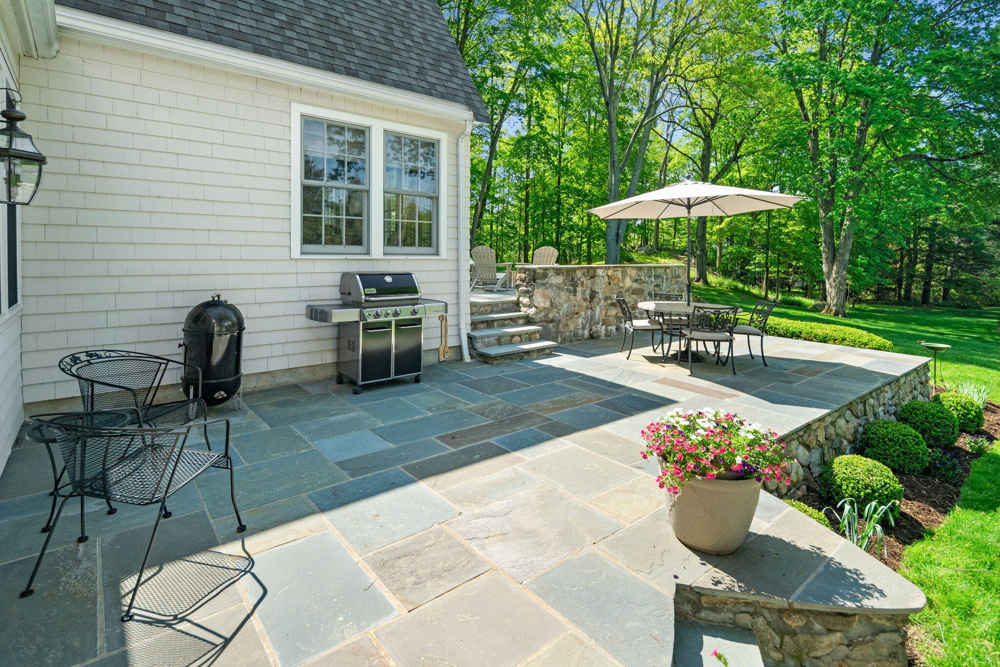 1466 Ponus Ridge Road New Canaan, CT 06840 - Photo 72 of 81 a view of a backyard with table and chairs under an umbrella with a barbeque grill and potted plants
