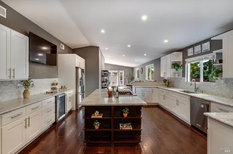 a large kitchen with stainless steel appliances kitchen island granite countertop a large stove a sink dishwasher and white cabinets with wooden floor