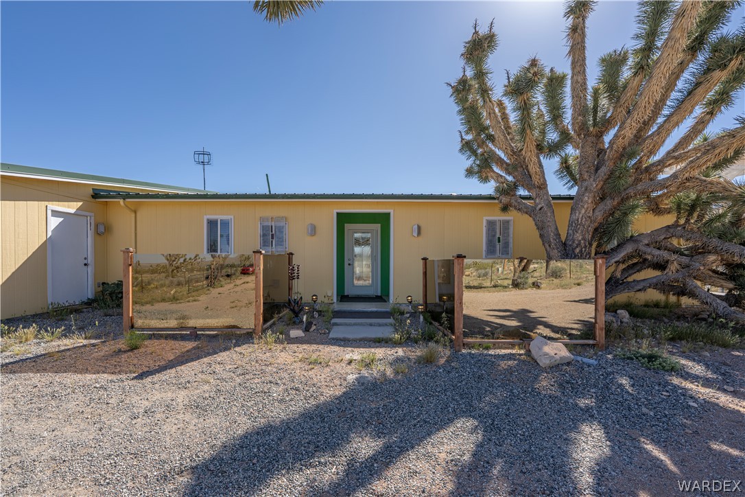 26512 North Yucca Road Meadview, AZ 86444 - Photo 10 of 38 Exterior view of the property featuring a yellow facade, a green front door, and an extensive gravel yard with a large desert tree