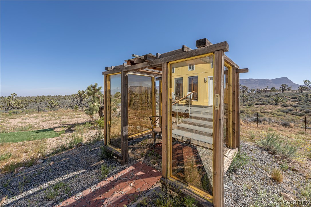 26512 North Yucca Road Meadview, AZ 86444 - Photo 16 of 38 The property features a yellow exterior and an outdoor structure with glass panels, offering views of the surrounding landscape and mountains in the distance
