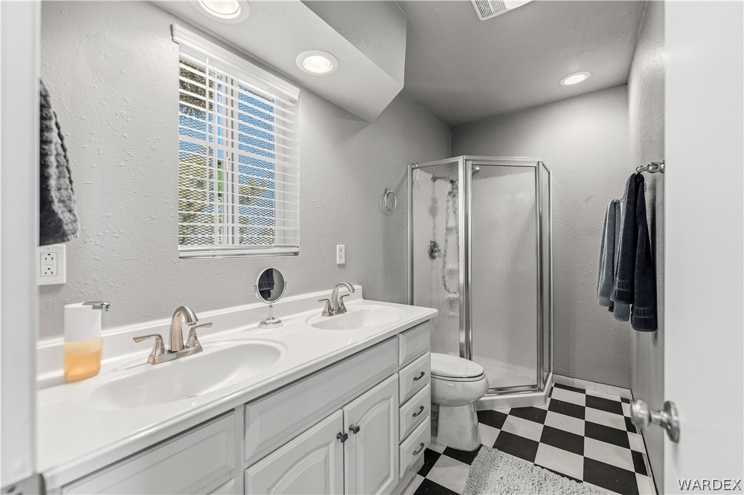 26512 North Yucca Road Meadview, AZ 86444 - Photo 30 of 38 The bathroom features a double vanity with white cabinetry, a corner shower, and a window with blinds