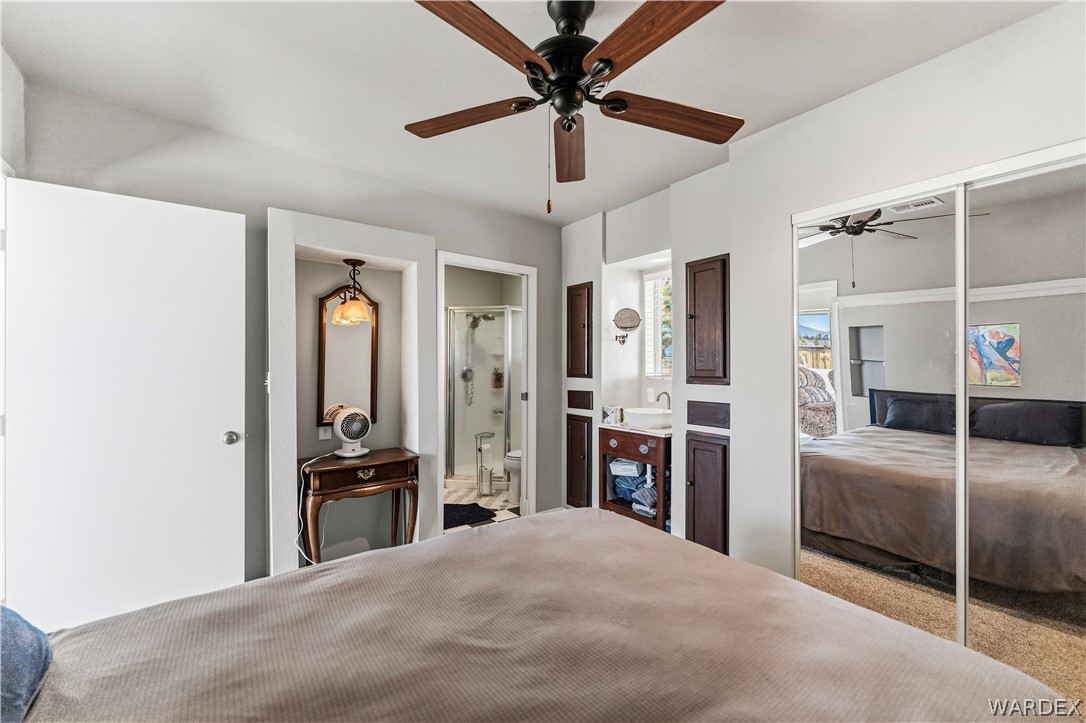 26512 North Yucca Road Meadview, AZ 86444 - Photo 32 of 38 Bedroom featuring a ceiling fan, mirrored closet doors, and built-in cabinetry with a sink and window