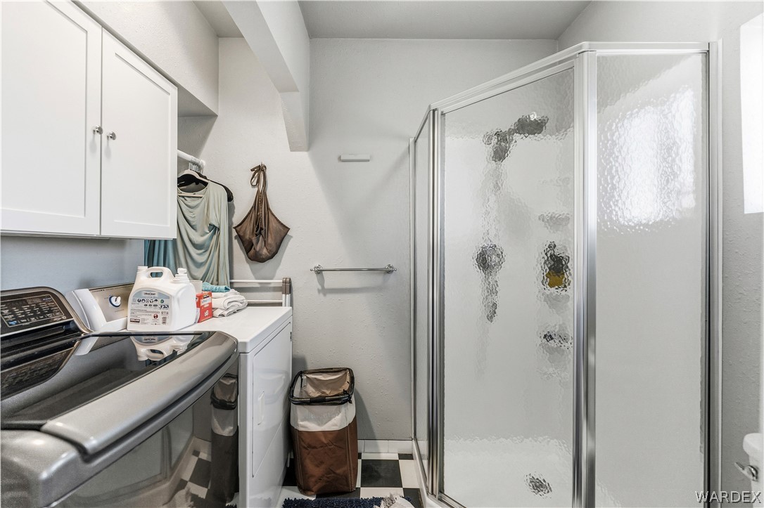 26512 North Yucca Road Meadview, AZ 86444 - Photo 33 of 38 This utility space features white cabinetry, a washer and dryer, and a corner shower with a frosted glass enclosure