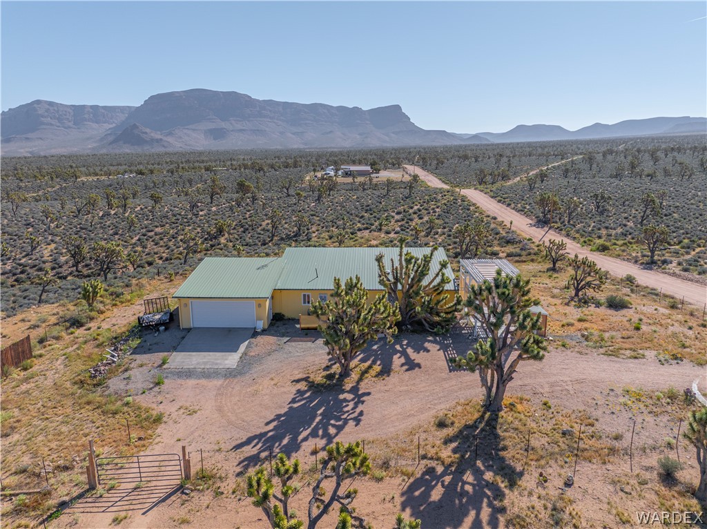 26512 North Yucca Road Meadview, AZ 86444 - Photo 5 of 38 The property features a single-story residence with a light-colored exterior and a green roof, set within a vast desert landscape with numerous trees and mountainous terrain in the distance