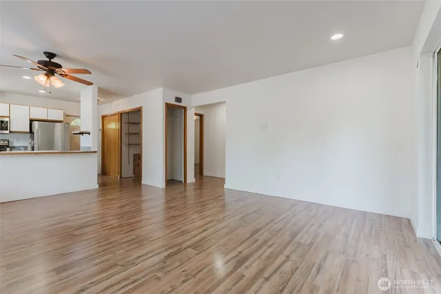 a view of an empty room with wooden floor and a kitchen