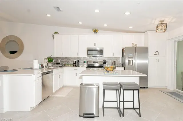 a kitchen with stainless steel appliances kitchen island granite countertop a refrigerator a stove and white cabinets with wooden floors