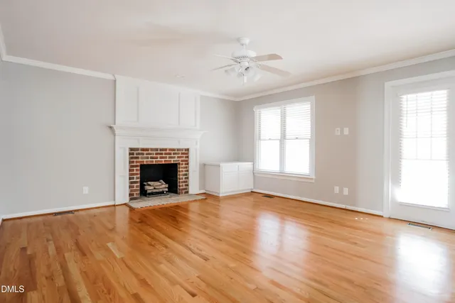 a view of an empty room with wooden floor fireplace and a window