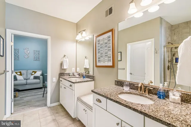 a bathroom with a granite countertop double vanity sink a mirror and a shower