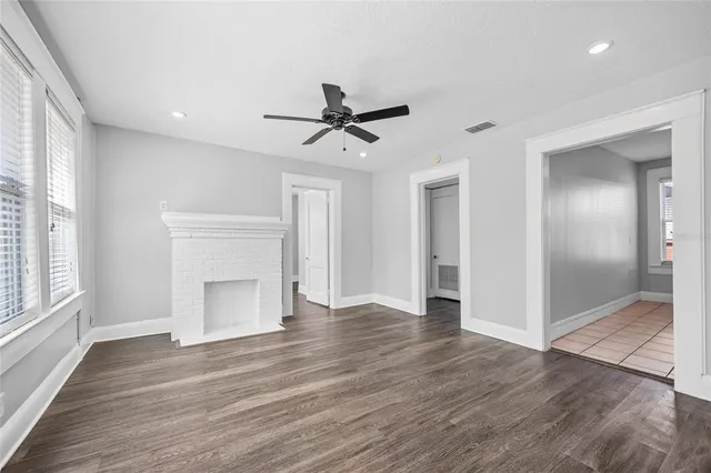 an empty room with wooden floor a ceiling fan and windows