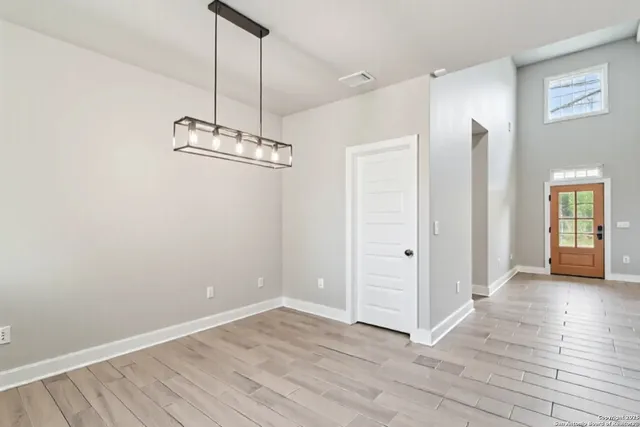 an empty room with wooden floor a chandelier and windows