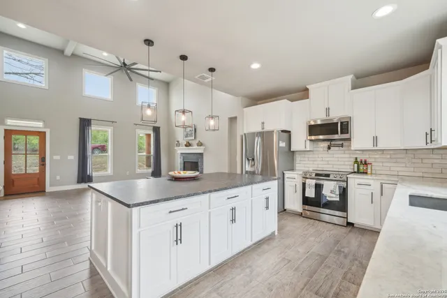 a kitchen with stainless steel appliances granite countertop a sink dishwasher a refrigerator and a oven with white cabinets