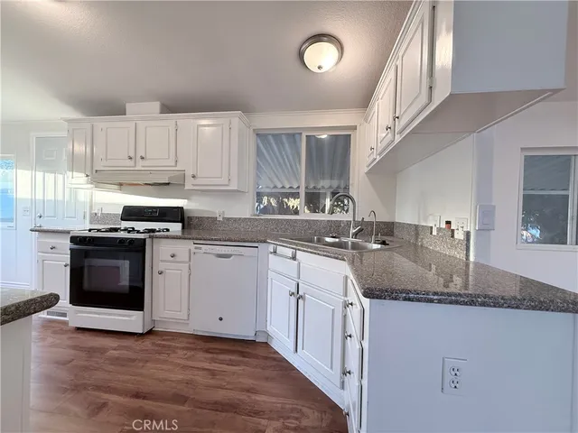 a kitchen with granite countertop a sink dishwasher a stove and a refrigerator with wooden floor