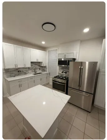a kitchen with granite countertop a refrigerator a sink and white cabinets