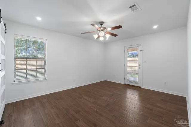 an empty room with wooden floor chandelier fan and windows