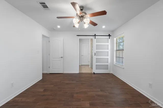 an empty room with wooden floor chandelier fan and windows