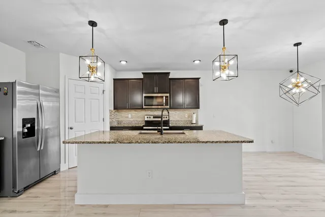 a kitchen with stainless steel appliances granite countertop a sink a refrigerator and a wooden floor