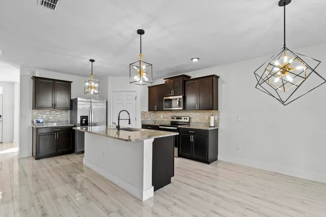 a kitchen with stainless steel appliances granite countertop a stove top oven a sink dishwasher a refrigerator and a dining table with wooden floor