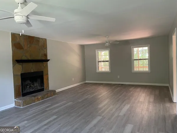 a view of an empty room with wooden floor fireplace and a window