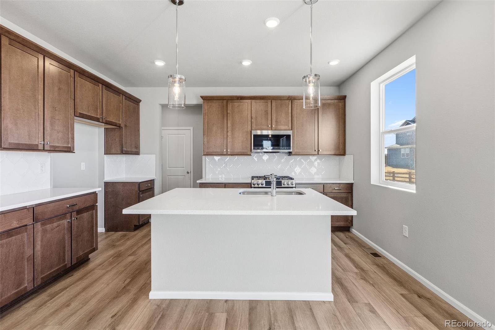 15293 Olive Way Thornton, CO 80602 - Photo 2 of 29 a kitchen with kitchen island a sink wooden floor and white appliances