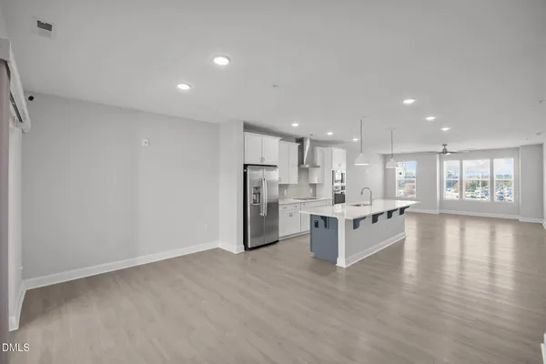 a large white kitchen with kitchen island a refrigerator a sink dishwasher a oven and a dining table with wooden floor