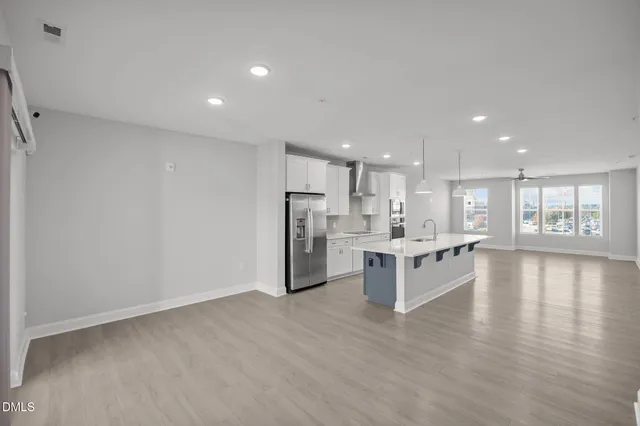 a large white kitchen with kitchen island a refrigerator a sink dishwasher a oven and a dining table with wooden floor