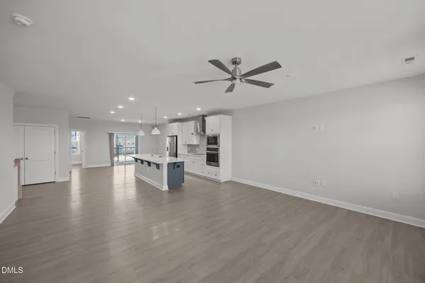 a view of an empty room with kitchen and window