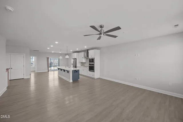 a view of an empty room with kitchen and window