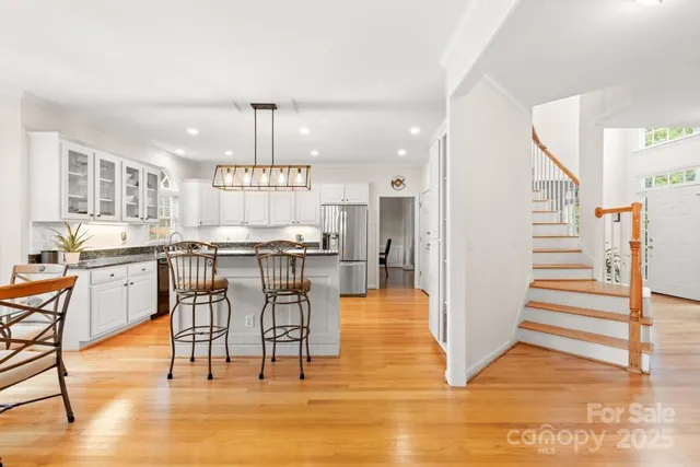 a kitchen with stainless steel appliances kitchen island granite countertop a refrigerator a stove a dining table and chairs with wooden floor