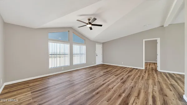 an empty room with wooden floor ceiling fan and windows