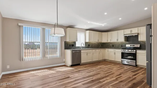 a kitchen with granite countertop a refrigerator oven a sink dishwasher and white cabinets with wooden floor