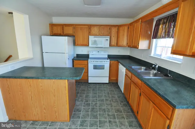 a kitchen with granite countertop a sink a stove top oven a counter space and cabinets