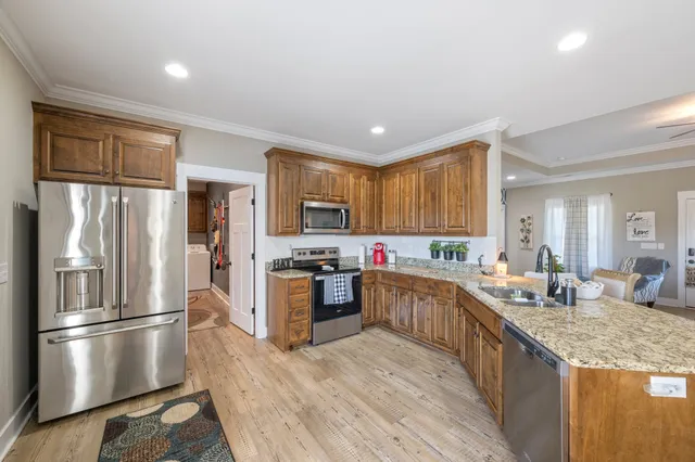 a kitchen with stainless steel appliances granite countertop a refrigerator a sink dishwasher a stove and white countertops with wooden floor