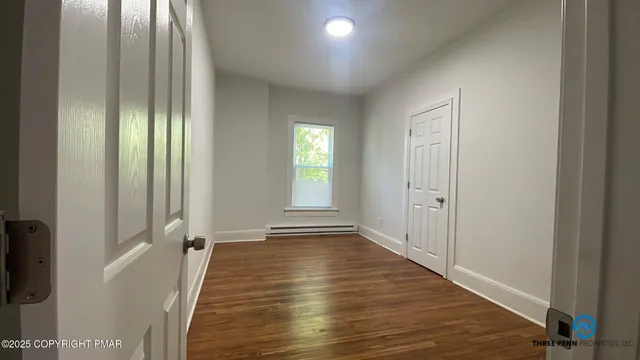 a view of an empty room with wooden floor and a window