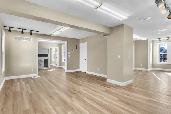 a view of an empty room with wooden floor and a kitchen