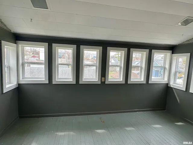 an empty room with wooden floor fan and windows