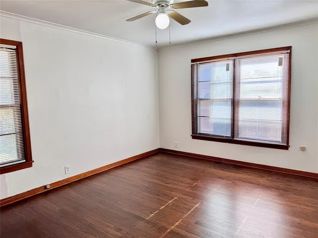 an empty room with wooden floor chandelier fan and windows